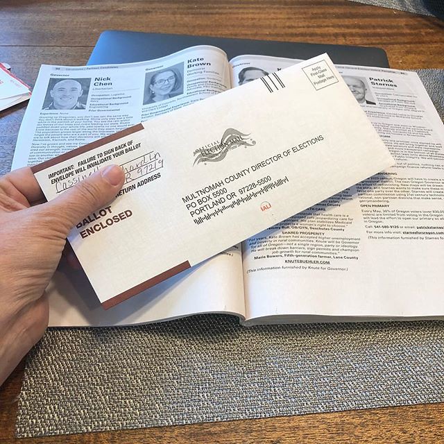 Hand holding an Oregon vote-by-mail envelope over an election guide.