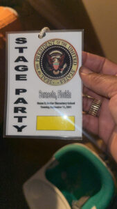 A hand holding a laminated pass that reads "Stage Party" with a Presidential seal.