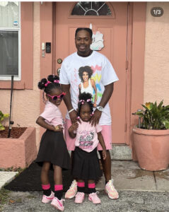 Andre Hobbs Jr. and his two daughters smiling outside their home.