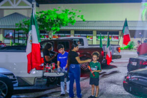 Two kids and two adults in an attendance at a party in a parking lot. Mexican flags abound.