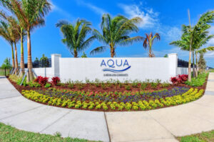 Aqua sign surrounded by flowers and palm trees.