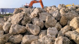 A massive pile of rocks along the shore near construction equipment.
