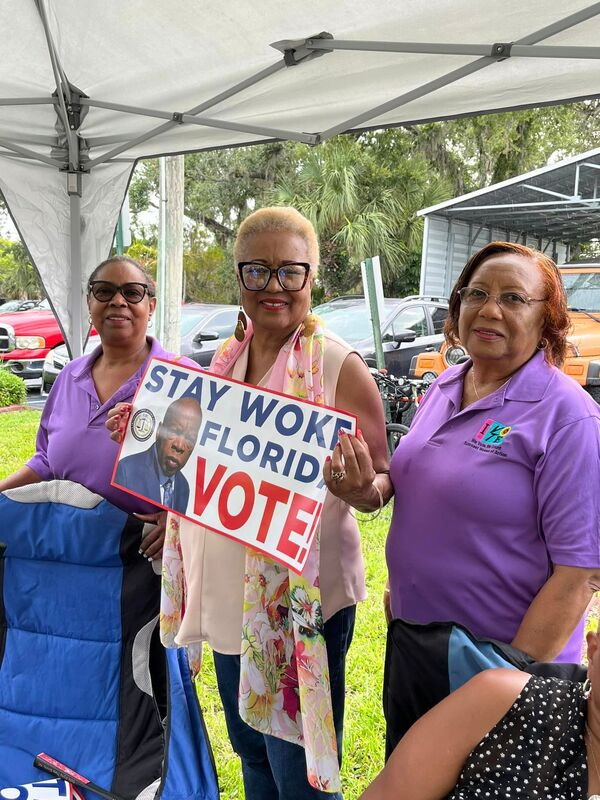 Helen James smiling and holding a sign that reads "Stay woke, Florida; Vote" alongside two other volunteers.