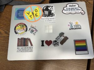 A laptop covered in stickers including a rainbow pride flag and a butterfly with the word "VOTE" written on its wings.