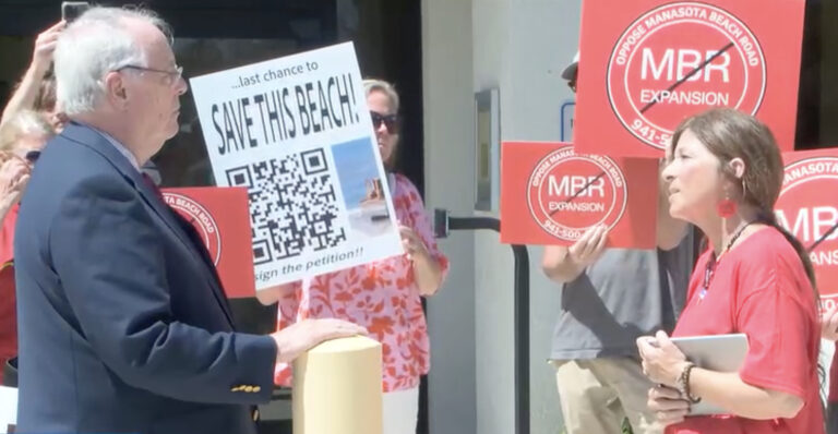 Pat Neal and Kelly Bauman speak to one another while demonstrators surround them with signs opposing the MBR Expansion.