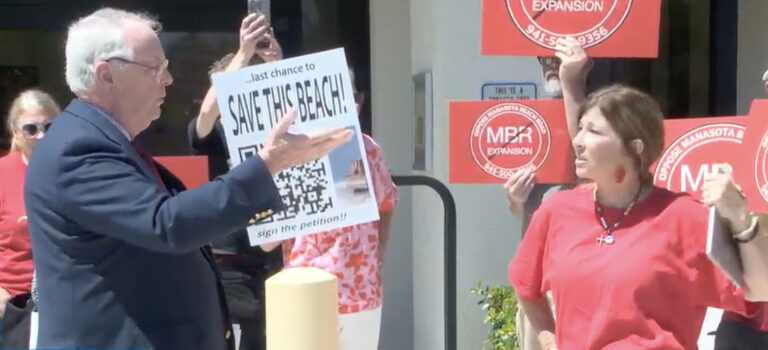 Pat Neal and Kelly Bauman speak to one another while demonstrators surround them with signs opposing the MBR Expansion.