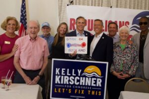 Several smiling people surrund Kelly Kirschner, who holds up a sign with a line fading from blue to purple to red which reads "Either or" on the top and "both and" on the bottom.