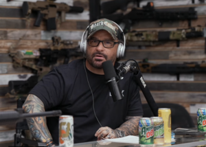 Will Meade in a studio in front of a wall lined with guns.