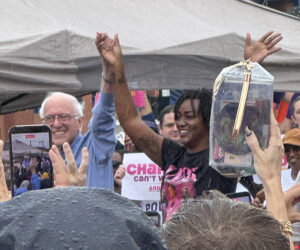 Bernie Sanders and Angie Nixon raise their hands triumphantly amid a dense crowd of supporters.