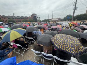 A full crowd of people with umbrellas in front of a small stage.