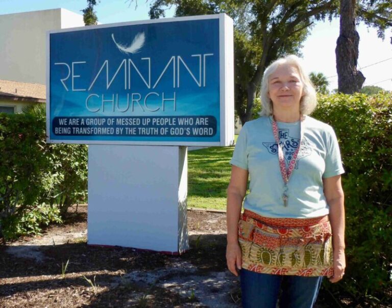 Tammy Burns smiling standing next to a sign at the front of the Remnant Church.