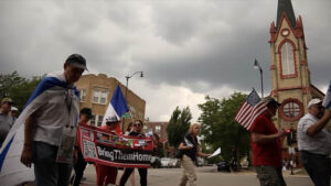 Run for Their Lives demonstrators, one of whom wears a flag of Israel draped over their shoulders as a cape, carry a banner that reads "Bring Them Home."