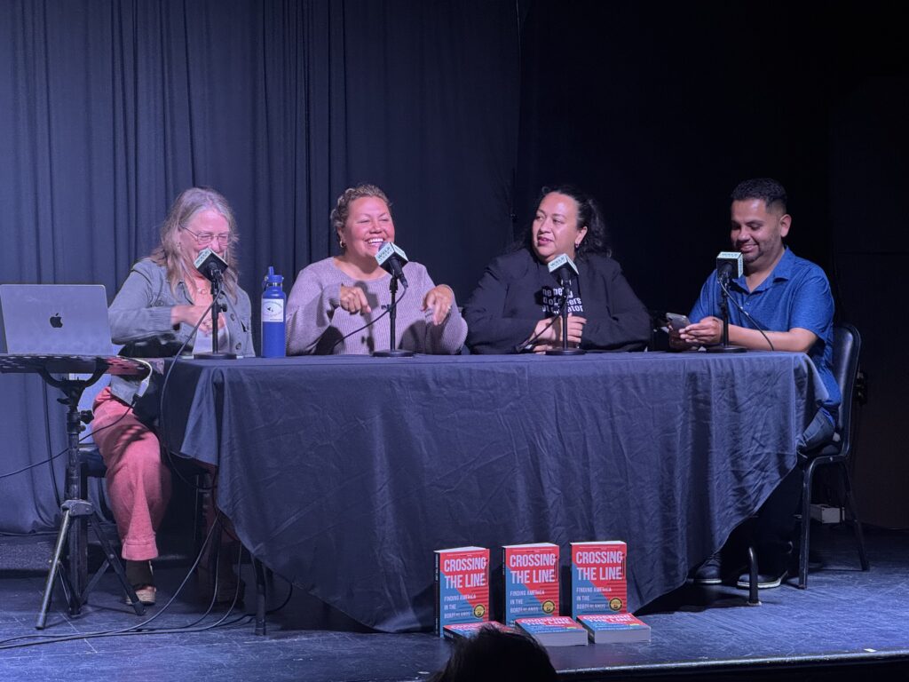 Sarah Towle, Michelle Jewell, Daniela Arcadia and Junior Salazar at a panel on stage. Six copies of the book Crossing the Line sit in front of their table.